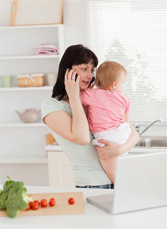 simsearch:400-04712944,k - Pretty brunette woman on the phone while holding her baby in her arms in the kitchen Stock Photo - Budget Royalty-Free & Subscription, Code: 400-04884718