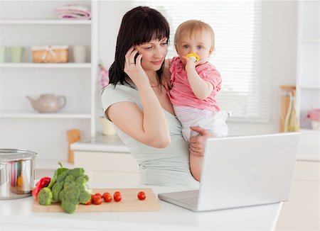simsearch:400-04712944,k - Good looking brunette woman on the phone while holding her baby in her arms in the kitchen Stock Photo - Budget Royalty-Free & Subscription, Code: 400-04884713