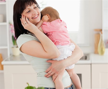 Lovely brunette woman on the phone while holding her baby in her arms in the kitchen Stock Photo - Budget Royalty-Free & Subscription, Code: 400-04884720