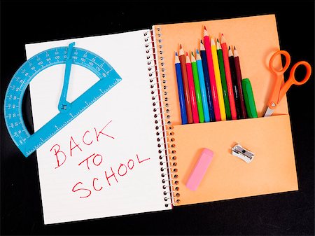 Spiral notebook for back-to-school with colored pencils, pens, scissors in pocket and protractor, eraser, and pencil sharpener on top. Isolated on black. Photographie de stock - Aubaine LD & Abonnement, Code: 400-04885033