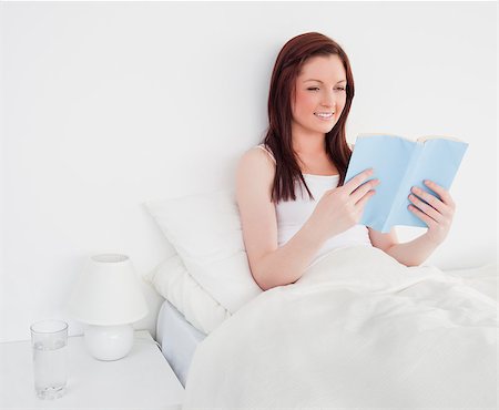 simsearch:400-04881612,k - Pretty red-haired woman reading a book while sitting on her bed Stock Photo - Budget Royalty-Free & Subscription, Code: 400-04881371