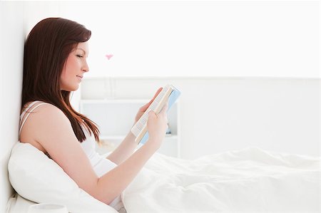 simsearch:400-04881612,k - Pretty red-haired female reading a book while sitting on her bed Stock Photo - Budget Royalty-Free & Subscription, Code: 400-04881487