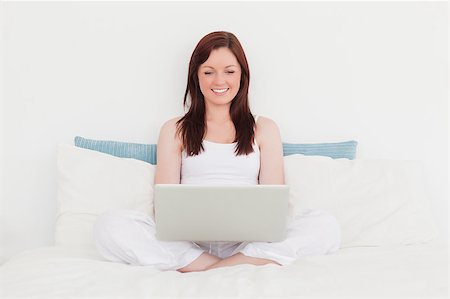 Gorgeous red-haired female relaxing with her laptop while sitting on her bed Stock Photo - Budget Royalty-Free & Subscription, Code: 400-04881499