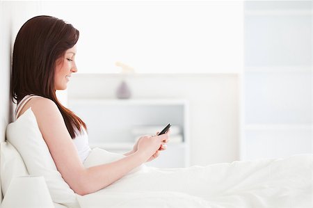 simsearch:6109-06194459,k - Attractive red-haired female writing a text on her mobile while sitting on her bed Foto de stock - Super Valor sin royalties y Suscripción, Código: 400-04881492