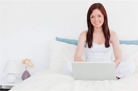 Attractive red-haired woman relaxing with her laptop while sitting on her bed Stock Photo - Budget Royalty-Free & Subscription, Code: 400-04881504
