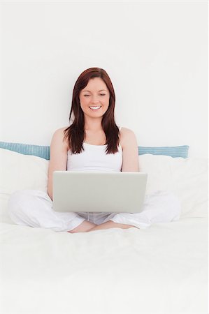 Cute red-haired female relaxing with her laptop while sitting on her bed Stock Photo - Budget Royalty-Free & Subscription, Code: 400-04881501