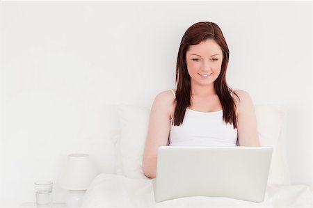 Good looking red-haired woman relaxing with her laptop while sitting on her bed Stock Photo - Budget Royalty-Free & Subscription, Code: 400-04881616
