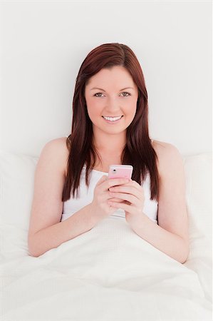 simsearch:400-04881612,k - Good looking red-haired woman writing a text on her mobile while sitting on her bed Stock Photo - Budget Royalty-Free & Subscription, Code: 400-04881621