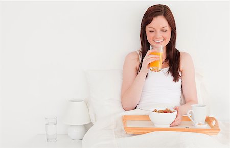 simsearch:400-04881612,k - Beautiful red-haired female drinking a glass of orange juice while sitting on her bed Stock Photo - Budget Royalty-Free & Subscription, Code: 400-04881639