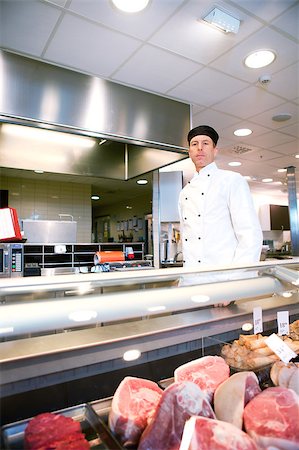 A serious satisfied butcher behind a fresh meat counter in a deli Photographie de stock - Aubaine LD & Abonnement, Code: 400-04882417