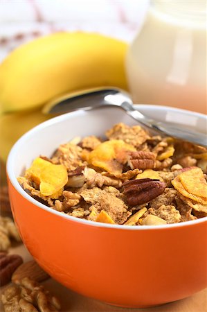 simsearch:400-04891088,k - Healthy and delicious breakfast with a bowl full of wholewheat flakes mixed with banana chips, walnuts and pecan nuts surrounded by nuts and fresh banana with milk in a jug in the back (Selective Focus, Focus on the pecan nut one third into the bowl) Stock Photo - Budget Royalty-Free & Subscription, Code: 400-04891088
