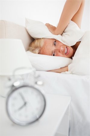 simsearch:6109-06194402,k - Portrait of a tired woman hidding her head in a pillow while the alarmclock is ringing in her bedroom Stock Photo - Budget Royalty-Free & Subscription, Code: 400-04906019
