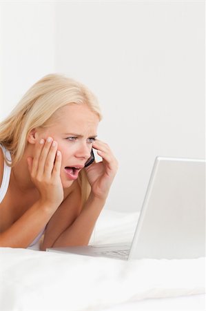 simsearch:400-05737165,k - Portrait of an upset woman on the phone while using a laptop in her bedroom Stock Photo - Budget Royalty-Free & Subscription, Code: 400-04903795