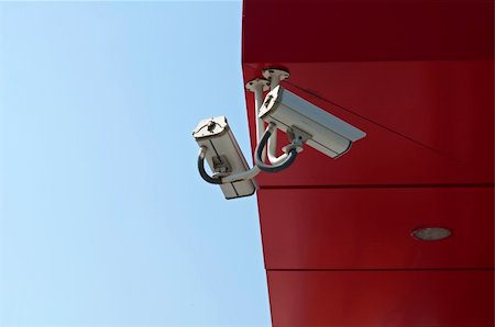 surveillance camera - Two surveillance Cameras on blue sky and red wall background Photographie de stock - Aubaine LD & Abonnement, Code: 400-04914914