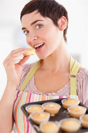 simsearch:400-05749772,k - Charming brunette woman showing muffins while eating one in a kitchen Stock Photo - Budget Royalty-Free & Subscription, Code: 400-04910954