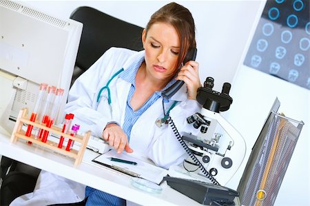 simsearch:400-04390415,k - Concerned medical doctor woman talking on phone and looking in clipboard Stock Photo - Budget Royalty-Free & Subscription, Code: 400-04925805