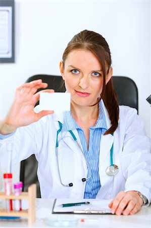 simsearch:400-04925813,k - Authoritative medical doctor woman sitting at office table and holding blank business card Stock Photo - Budget Royalty-Free & Subscription, Code: 400-04925815