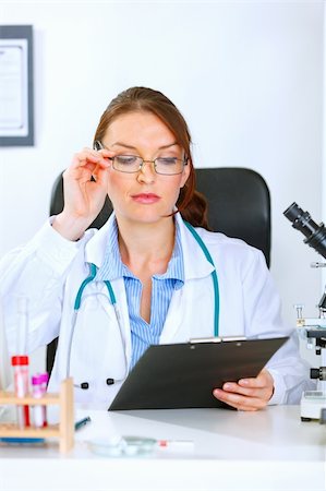 simsearch:400-04925813,k - Medical doctor woman sitting at office table and looking in clipboard Stock Photo - Budget Royalty-Free & Subscription, Code: 400-04925816