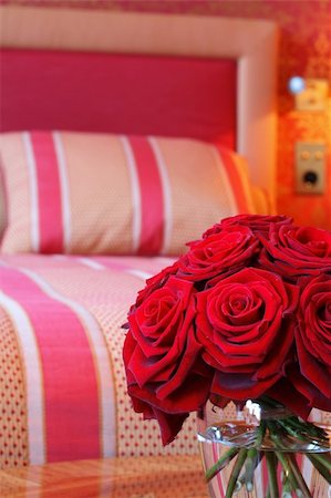 simsearch:400-04527694,k - A vase full of red roses in a clear glass vase on a wooden table against a background with a comfy bed. Foto de stock - Royalty-Free Super Valor e Assinatura, Número: 400-04939329