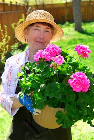 simsearch:400-04439731,k - Smiling senior woman holding a pot with flowers in her garden Photographie de stock - Aubaine LD & Abonnement, Code: 400-04946485