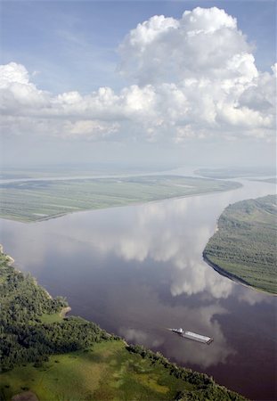 Warm summer day. White clouds are reflected in the specular it ironed great river. Small launch pushes large barge. Fotografie stock - Microstock e Abbonamento, Codice: 400-04942730