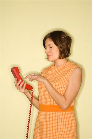 simsearch:400-04451365,k - Pretty Caucasian mid-adult woman wearing orange dress standing dialing red telephone. Foto de stock - Super Valor sin royalties y Suscripción, Código: 400-04956225