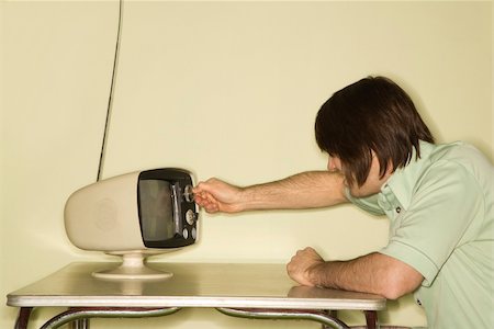 Side view of Caucasian mid-adult man sitting at 50's retro dinette set turning old television knob. Stock Photo - Budget Royalty-Free & Subscription, Code: 400-04956230