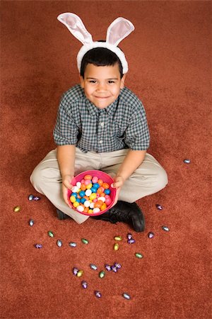 simsearch:400-04452450,k - Hispanic boy wearing bunny ears sitting on floor holding a bowl of chocolate candy eggs  with more candy scattered around him looking up at viewer smiling. Stock Photo - Budget Royalty-Free & Subscription, Code: 400-04957393