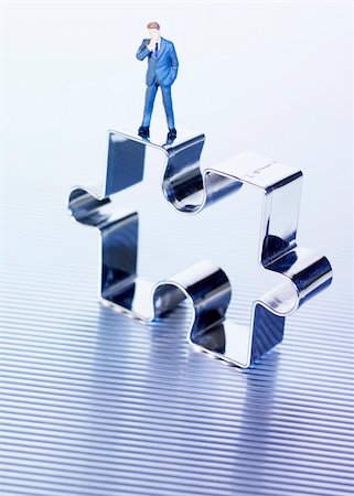 Stainless steel or meatl puzzle piece on ribbed surface with small toy man standing on top with hand on chin Stock Photo - Budget Royalty-Free & Subscription, Code: 400-04950663