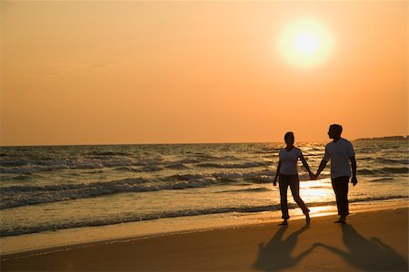 simsearch:400-03943979,k - Caucasian mid-adult couple holding hands and walking down beach at sunset. Foto de stock - Super Valor sin royalties y Suscripción, Código: 400-04953715