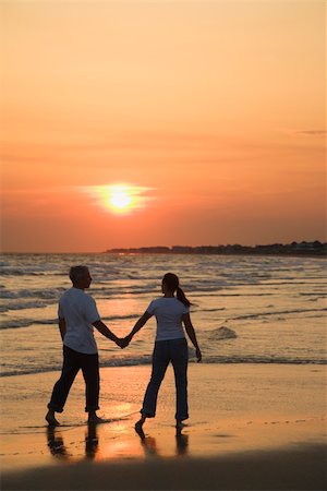 simsearch:400-03943979,k - Mid-adult couple holding hands and walking on beach at sunset. Foto de stock - Super Valor sin royalties y Suscripción, Código: 400-04953716