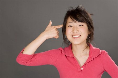 simsearch:400-04960190,k - Portrait of a beautiful Asian teenager posing on a gray background with finger pointing at head Photographie de stock - Aubaine LD & Abonnement, Code: 400-04960190