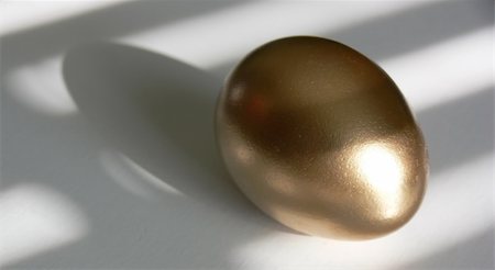 financial highlights - Golden egg on a white tabletop, with patterns of light and shadow laying across both. Taken with a Panasonic FZ30 Lumix. Stock Photo - Budget Royalty-Free & Subscription, Code: 400-04960781