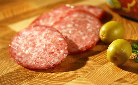 simsearch:400-05326789,k - Tasty fresh slices Salami. Beside there is some olives. A natural composition on a wooden table. Fotografie stock - Microstock e Abbonamento, Codice: 400-04975385