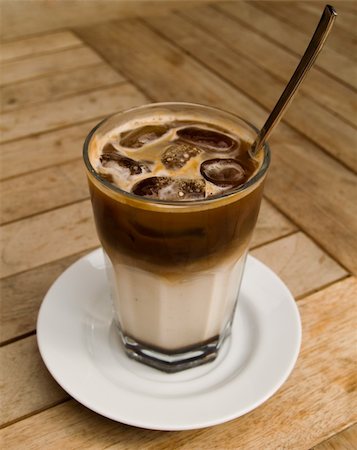 A shot of a glass of ice cold coffee on a wooden table. Front of the glass in focus. Foto de stock - Super Valor sin royalties y Suscripción, Código: 400-04978638