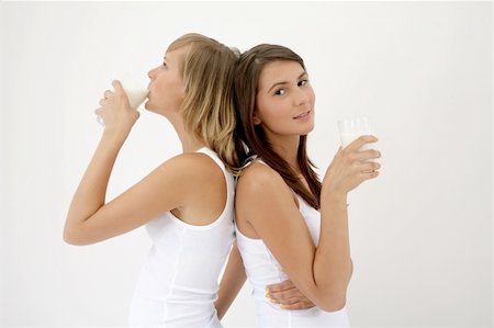 two girls standing back to back over white background, one drinking milk, other posing with glass of mik Photographie de stock - Aubaine LD & Abonnement, Code: 400-04984064