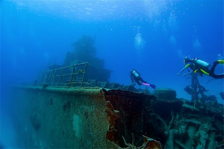 Two divers are swimming towards the superstructure of a shipwreck. Tangled wreckage in the foreground; the vessel recedes into the ocean blue in the background.  Space for copy above. Stock Photo - Budget Royalty-Free & Subscription, Code: 400-04997620