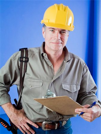 Construction worker with hard hat and clip board standing in front of a bright blue wall. Stock Photo - Budget Royalty-Free & Subscription, Code: 400-04993587