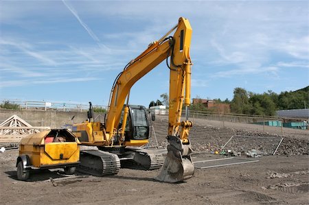 Industrial yellow digger standing idle on a building site with a small red diesel storage vehicle to the side. Set against a blue sky. Stock Photo - Budget Royalty-Free & Subscription, Code: 400-05014321