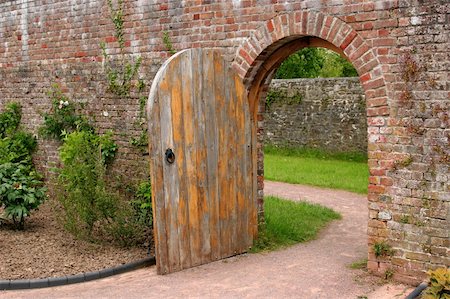 Old open arched wooden door set into an old red brick wall and leading to a grassed area beyond. Stock Photo - Budget Royalty-Free & Subscription, Code: 400-05012343