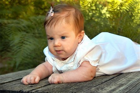 simsearch:400-04067084,k - Tiny infant lays on a wooden bridge.  She has her head up and is enjoying her first day at the park.  She has a pink bow in her hair and has on a light pink dress. Stock Photo - Budget Royalty-Free & Subscription, Code: 400-05025128