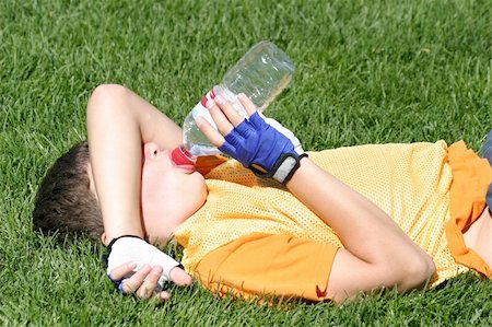 A tired athlete drinking a bottle of water during a break in soccer practice. The boy is lying downon the field to get some rest. Stock Photo - Budget Royalty-Free & Subscription, Code: 400-05025457