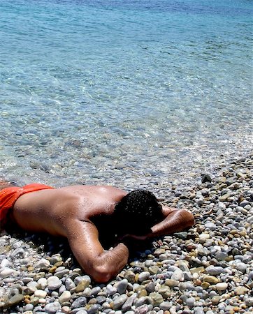 Young man laying on the beach, half in water, relaxing, holidays in Greece Stockbilder - Microstock & Abonnement, Bildnummer: 400-05020310