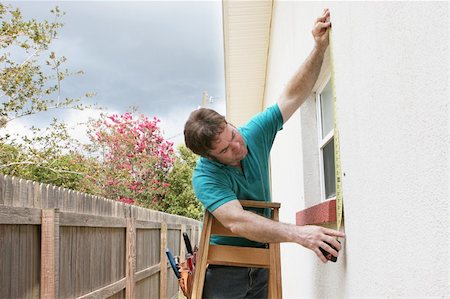 A carpenter measuring a window for hurricane shutters.  Dark storm clouds are overhead. Stock Photo - Budget Royalty-Free & Subscription, Code: 400-05021188