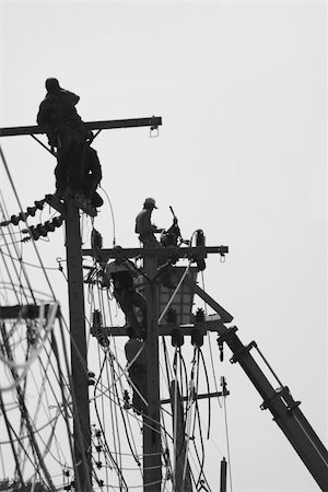 electricity pole silhouette - Silhouette men performing maintenance work on poles for electric wiring. Black and white photo with shallow depth of field. The second mast in focus. Foto de stock - Super Valor sin royalties y Suscripción, Código: 400-05023602