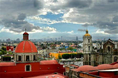 Church steeples, roof tops and mountains form the skyline of Mexico City.  Blue skles and grey clouds and smog cover top of photo. Foto de stock - Royalty-Free Super Valor e Assinatura, Número: 400-05030622