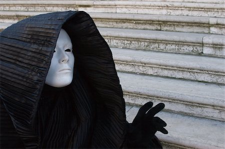 Figure in the black costume with hood, and white mask, gesturing on the stairs. Venice. Masquerade Foto de stock - Royalty-Free Super Valor e Assinatura, Número: 400-05031265