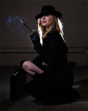 Beautiful blond woman wearing a black trenchcoat and black fedora style hat in a dark alley smoking a cigarette Stockbilder - Microstock & Abonnement, Bildnummer: 400-05033283