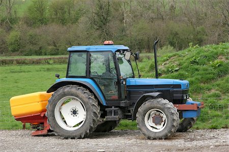 Blue tractor standing idle towing a yellow plastic fertiliser spreader. Rural farmland to the rear. Stock Photo - Budget Royalty-Free & Subscription, Code: 400-05045844