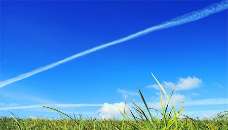 Celestial landscape. A reactive vapour trail is crossed by bright blue celestial space, flying above a juicy green grass which easy fluffy clouds rest on. Stock Photo - Budget Royalty-Free & Subscription, Code: 400-05040448